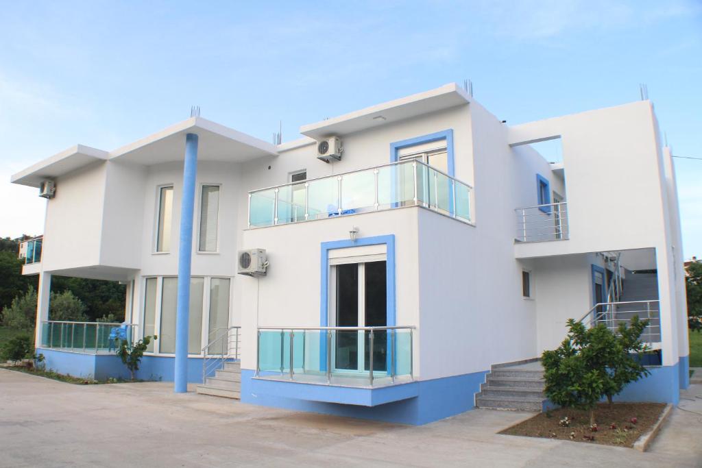a white house with blue columns and balconies at Gjinaj Apartments in Ulcinj