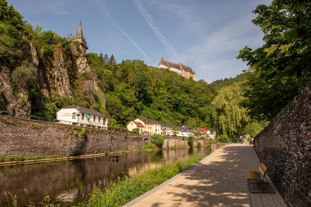 a walkway next to a river with a castle in the background at Hotel Belle Vue in Vianden