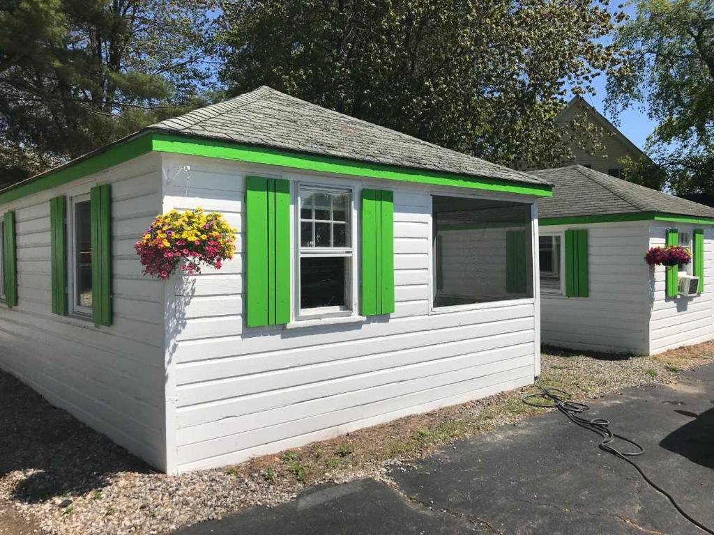a white and green building with green windows and flowers at Lighthouse Cabins in Old Orchard Beach
