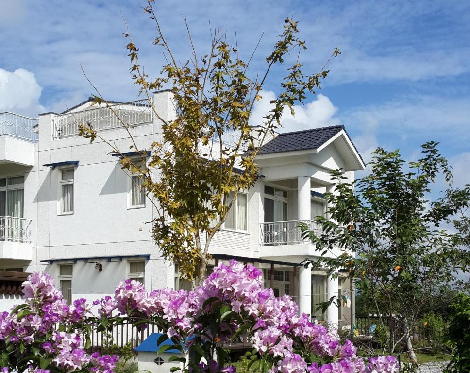 Un bâtiment blanc avec des fleurs violettes devant lui dans l'établissement Yi Tian Homestay, à Fengli