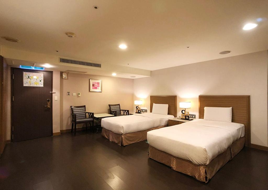 a hotel room with two beds and a table and chairs at Shihzuwan Hotel – Kaohsiung Station in Kaohsiung