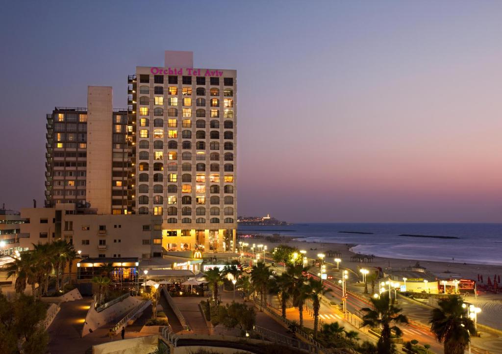 een hoog gebouw 's nachts met een stad en de oceaan bij Orchid Tel Aviv in Tel Aviv