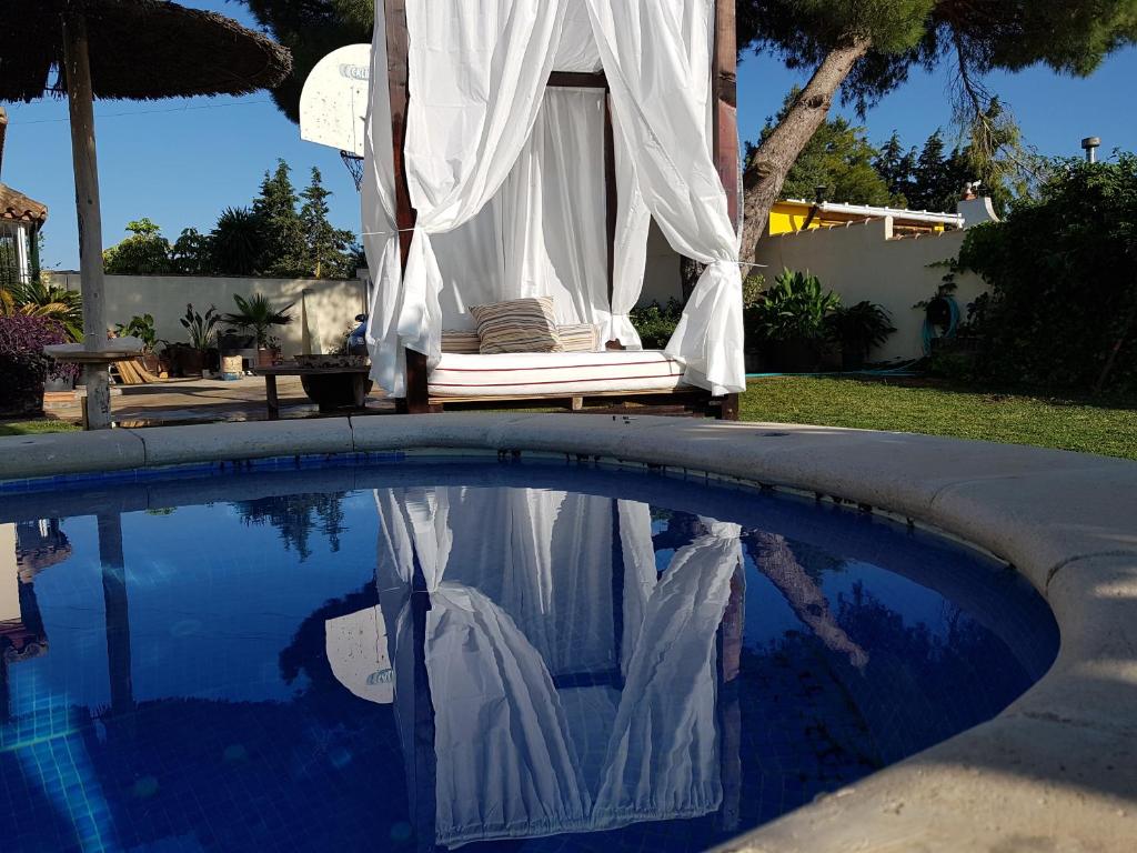 une chaise à baldaquin au-dessus d'une piscine avec sa réflexion dans l'eau dans l'établissement El chalet del Mar, à Chiclana de la Frontera