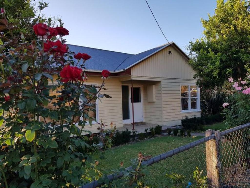 ein kleines Haus mit einem Zaun und roten Rosen in der Unterkunft Cottage on Main in Buchan