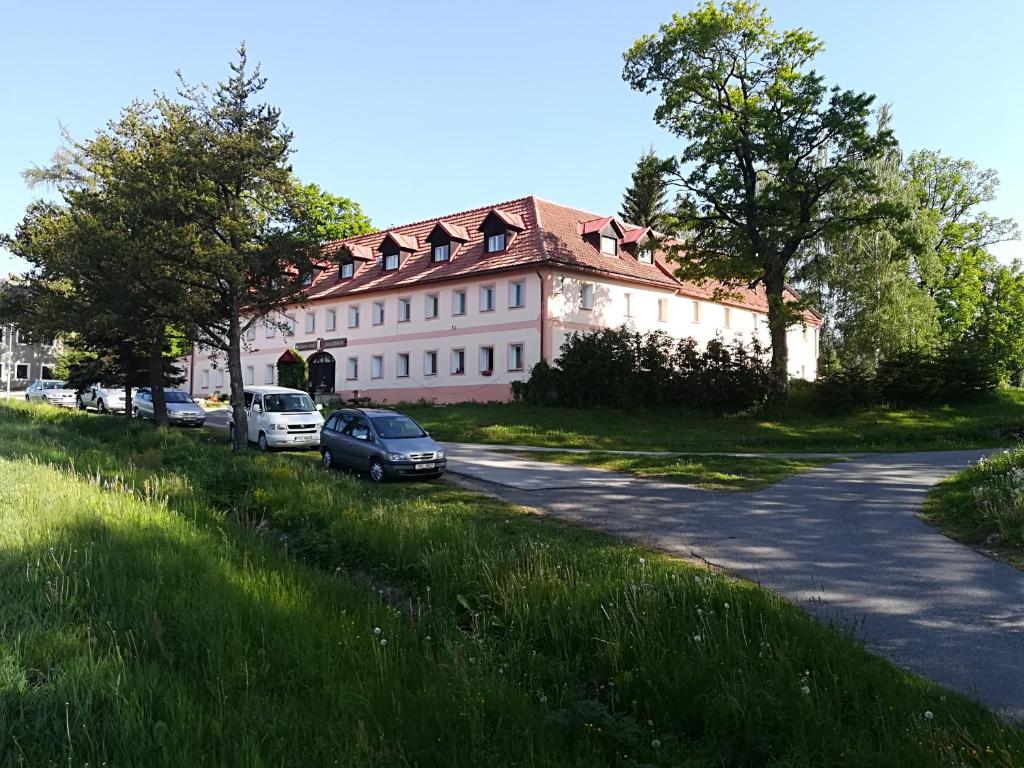 a large white building with cars parked on the side of a road at Penzion Tomy Pihlov in Horní Planá