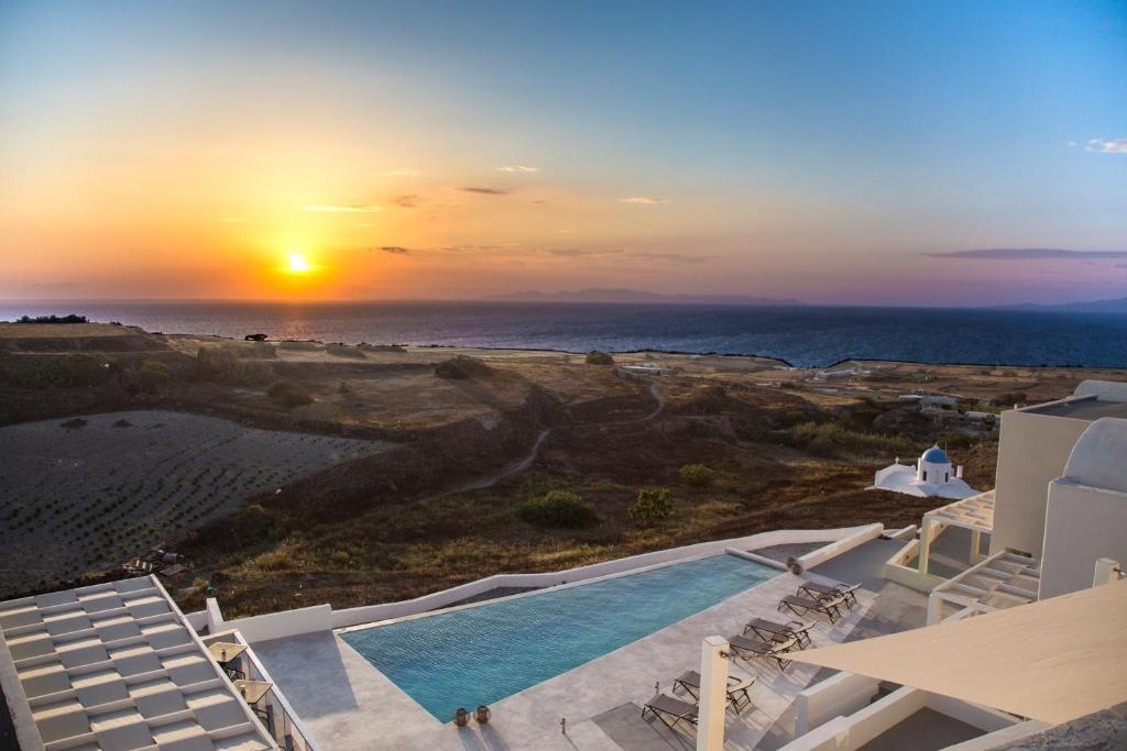 a sunset over a swimming pool and the ocean at Aplai Dome in Oia