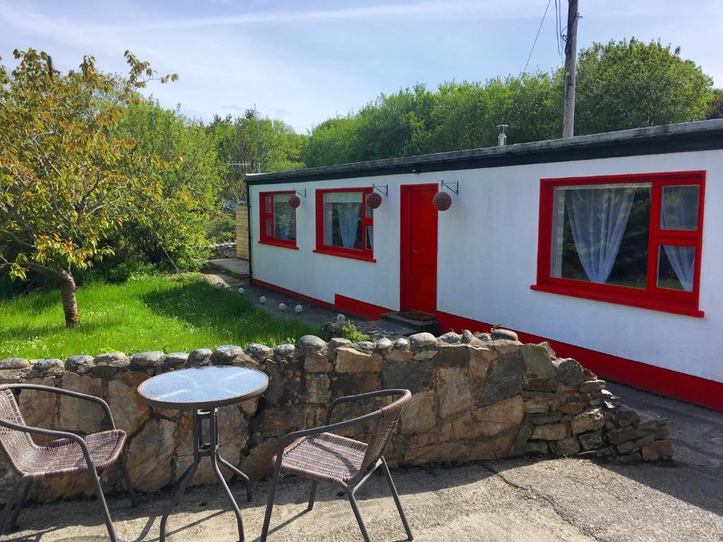 una pequeña casa con mesa y sillas junto a una pared de piedra en The Potters Cottage en Clifden