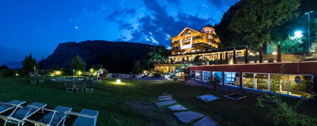 a large building with chairs in the grass at night at Alp Wellness Sport Hotel Panorama in Fai della Paganella