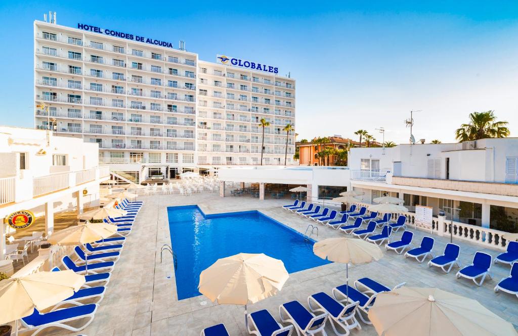 a pool with umbrellas and chairs and a hotel at Globales Condes de Alcudia in Port d'Alcudia