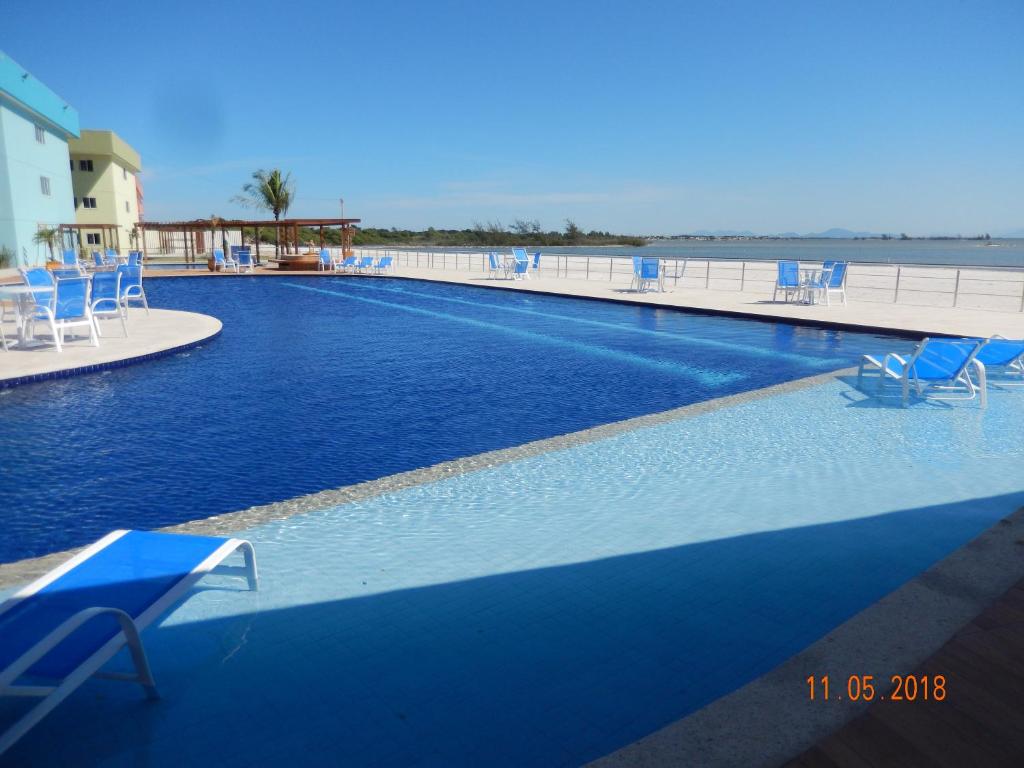 a large swimming pool with blue chairs and the ocean at Flat entre Mar e Lagoa in Arraial do Cabo