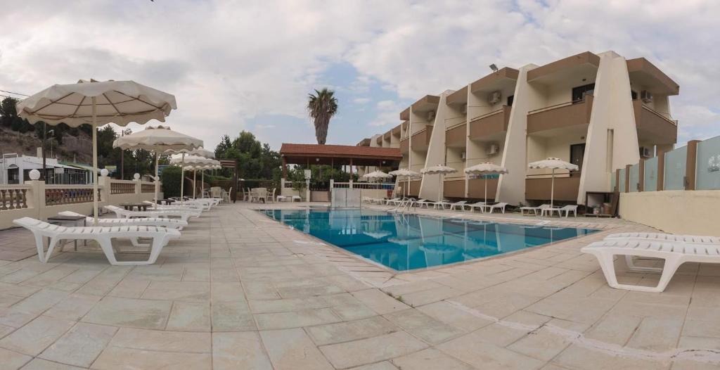 a resort with a pool with white chairs and umbrellas at Golden days in Afantou