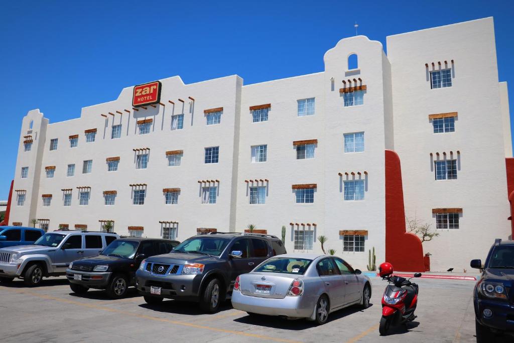 un gran edificio blanco con coches aparcados en un aparcamiento en Hotel Zar La Paz, en La Paz