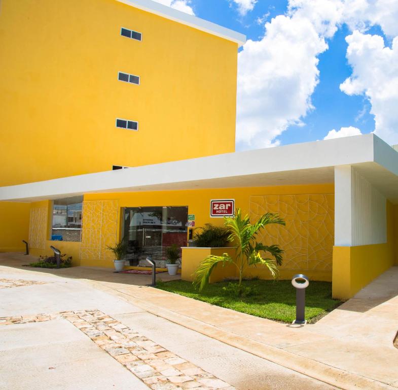 a yellow building with a palm tree in front of it at Hotel Zar Merida in Mérida