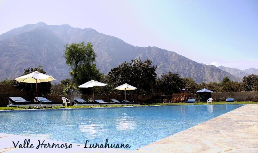 a swimming pool with chairs and umbrellas in front of a mountain at Hotel Vallehermoso Lunahuana in Lunahuaná