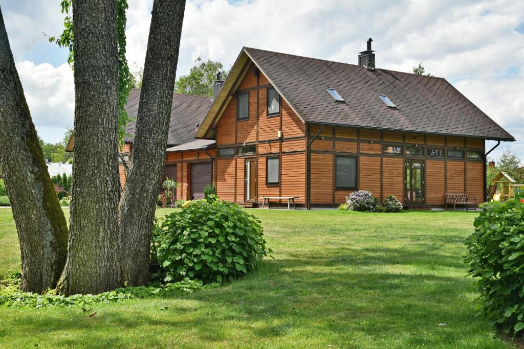 a large wooden house with a tree in the yard at Atostogų namelis Druskininkuose in Druskininkai