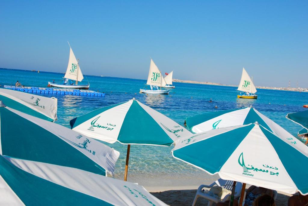 eine Gruppe von Sonnenschirmen am Strand mit Booten im Wasser in der Unterkunft Beau Site Hotel in Marsa Matruh