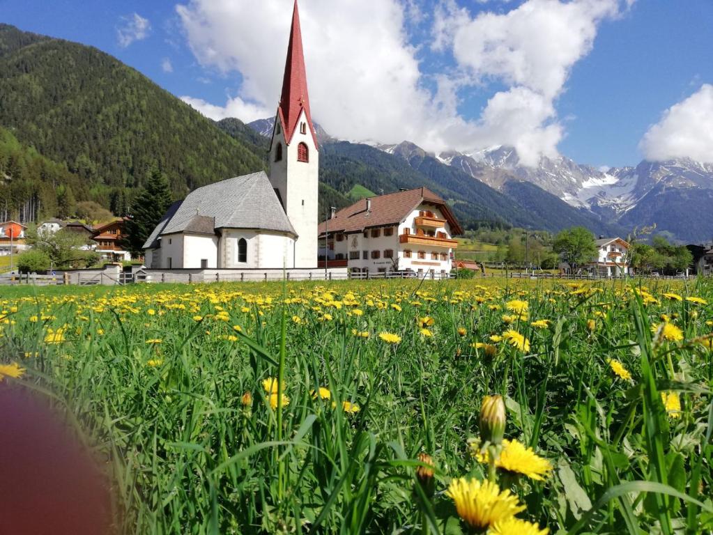 una iglesia con un campo de flores delante de ella en Hotel Messnerwirt en Anterselva di Mezzo