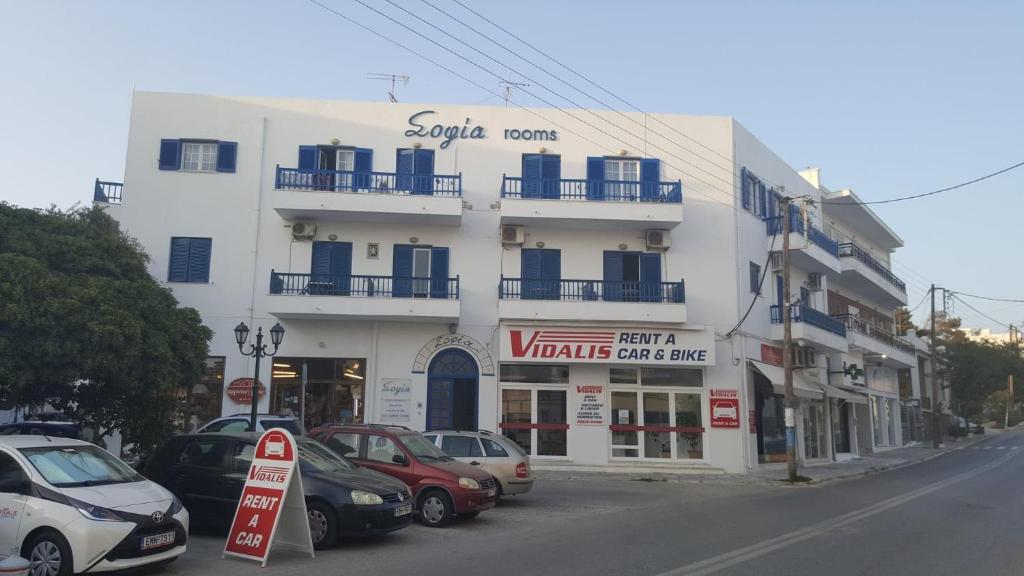 un bâtiment blanc avec des voitures garées devant lui dans l'établissement Sofia, à Tinos