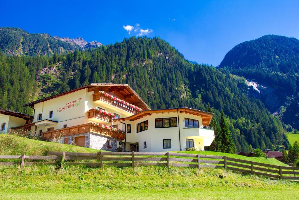 a building on a hill with mountains in the background at Pension Rosenhügel in Neustift im Stubaital
