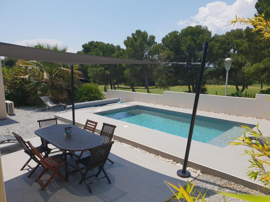 カップ・ダグドにあるCap d'agde Maison sur le golf avec piscine chauffée.のプールサイドのパティオ(テーブル、椅子付)