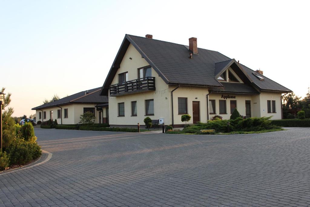ein weißes Haus mit schwarzem Dach auf einer Einfahrt in der Unterkunft Restauracja Applause in Ludwin
