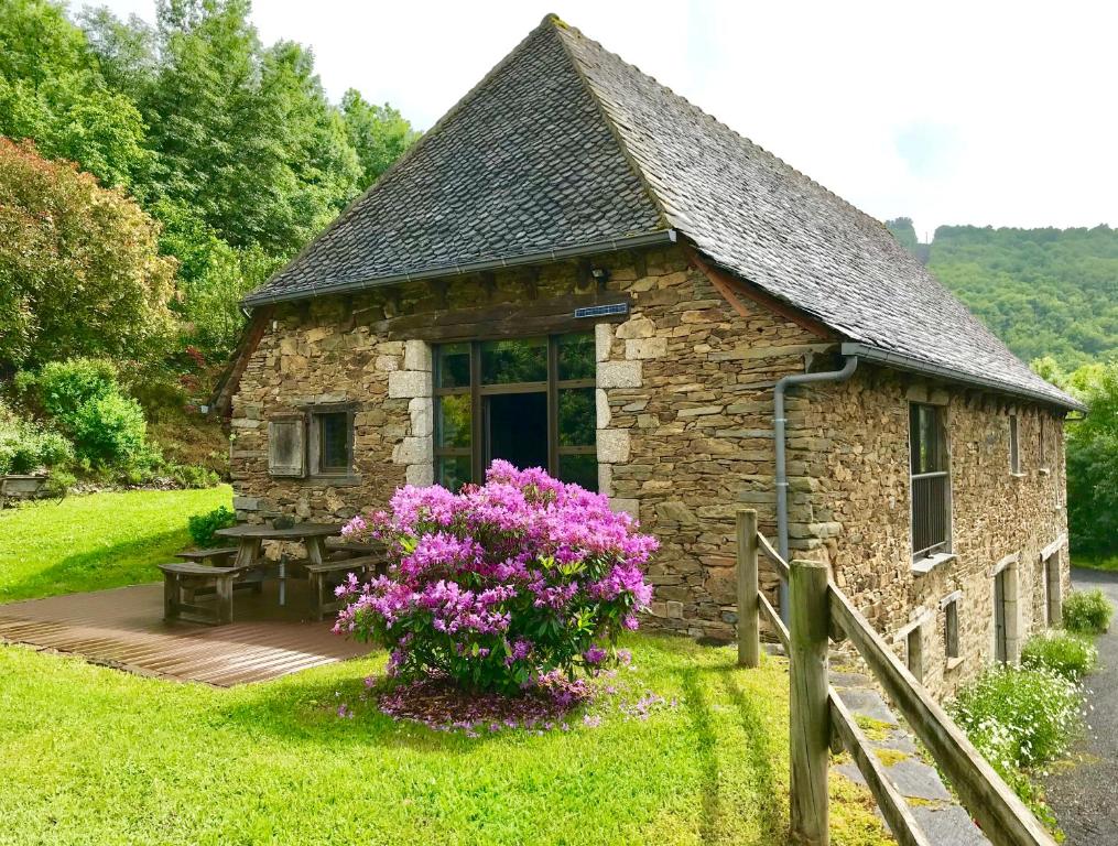 a small stone building with a table and purple flowers at LA PERLE DE LA VALLÉE in Vallon