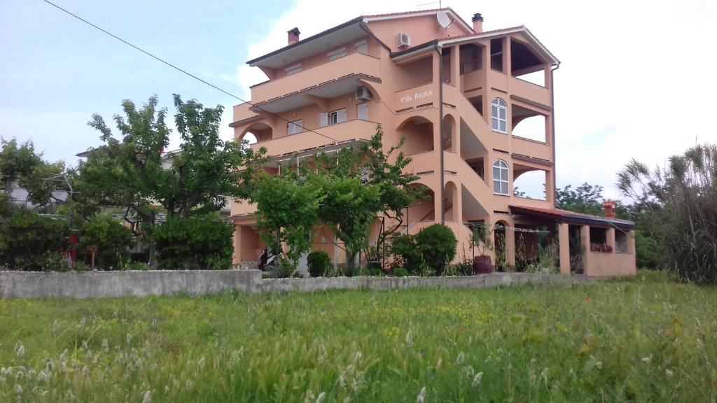 a large pink building on top of a green field at Apartments Rajka in Lopar