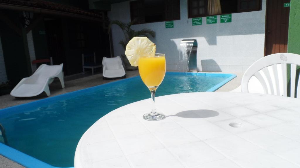 a glass of orange juice sitting on a table next to a pool at Pousada Rancho Verde in Porto Seguro