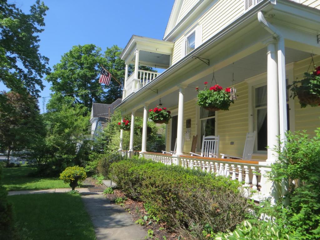 una casa amarilla con un porche con flores. en Cooperstown Bed and Breakfast en Cooperstown