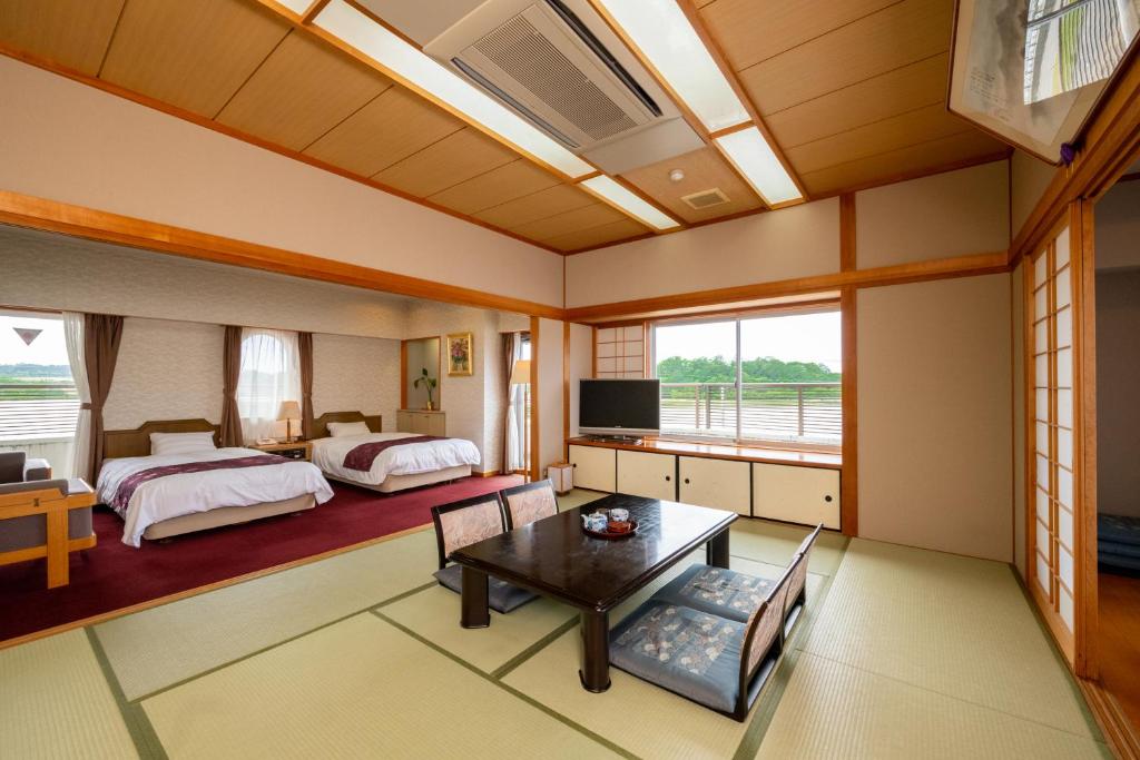 a large room with two beds and a table and a television at Awara Kitagata Onsen Kohanso Hana Yurari in Awara