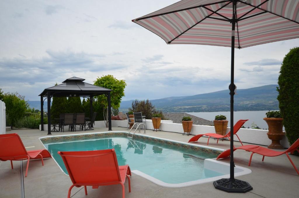 a swimming pool with chairs and an umbrella at Bella Luna Bed and Breakfast in West Kelowna