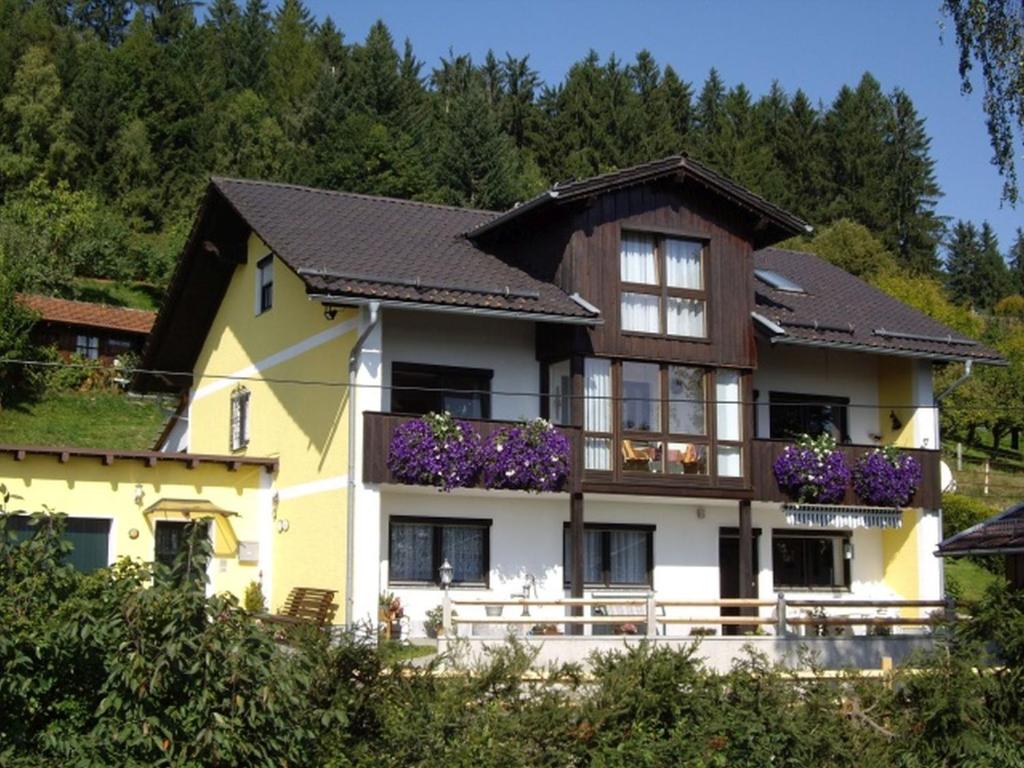 uma casa amarela e branca com flores roxas em Ferienwohnung Dorfblick (Herzog) em Lindberg