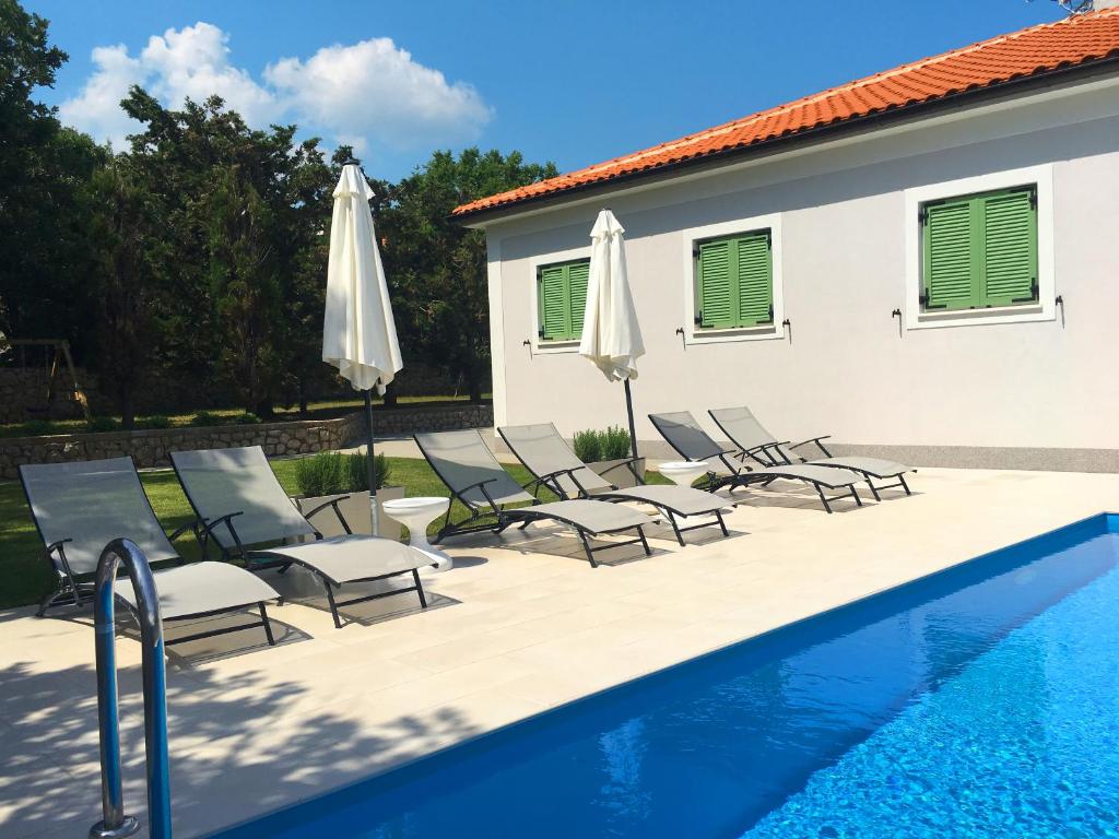 a pool with chairs and umbrellas next to a house at Villa Kvarner in Šilo