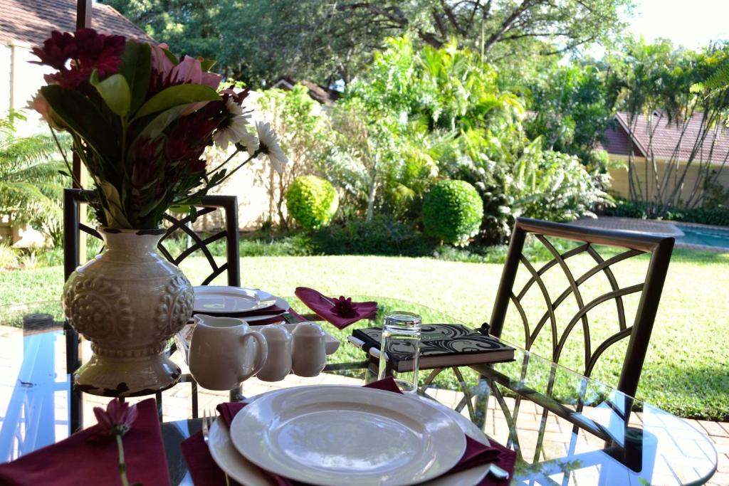 una mesa con platos y un jarrón con flores. en Cycas Guest House, en Malelane