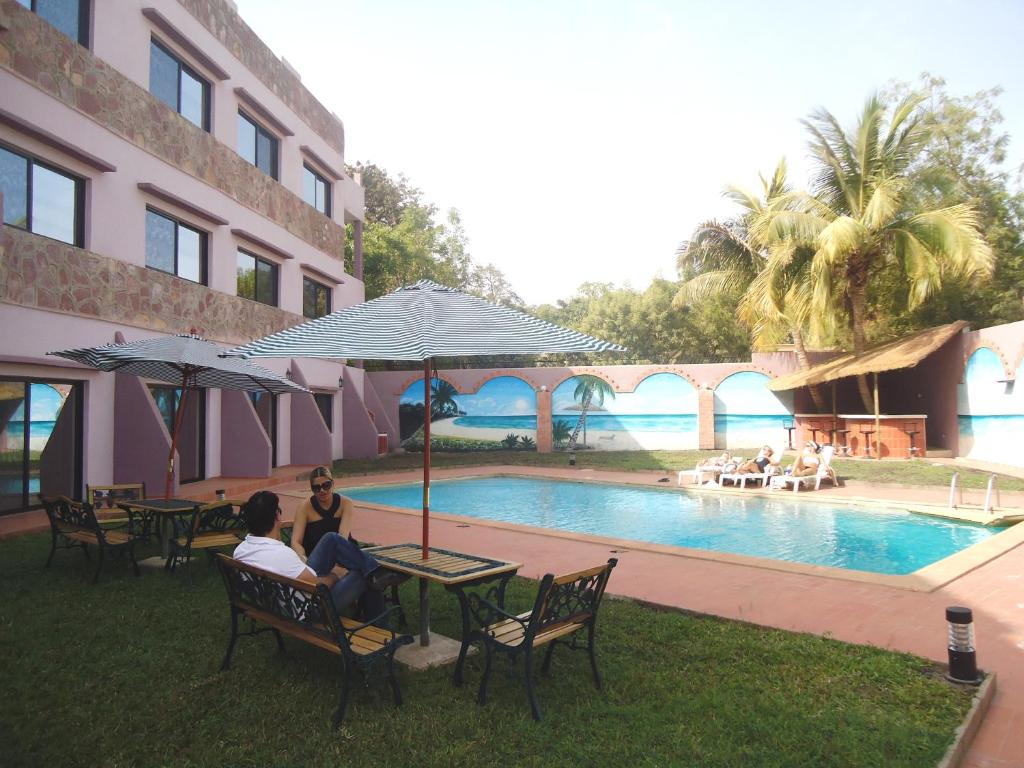 duas pessoas sentadas debaixo de um guarda-chuva ao lado de uma piscina em Le Relais de Bamako em Bamako