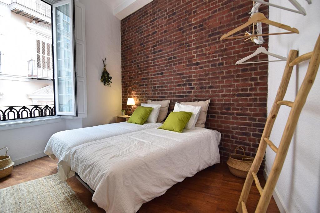 馬拉加的住宿－BRUNO´S HOME (OLD TOWN)，一间卧室设有砖墙和一张带绿色枕头的床