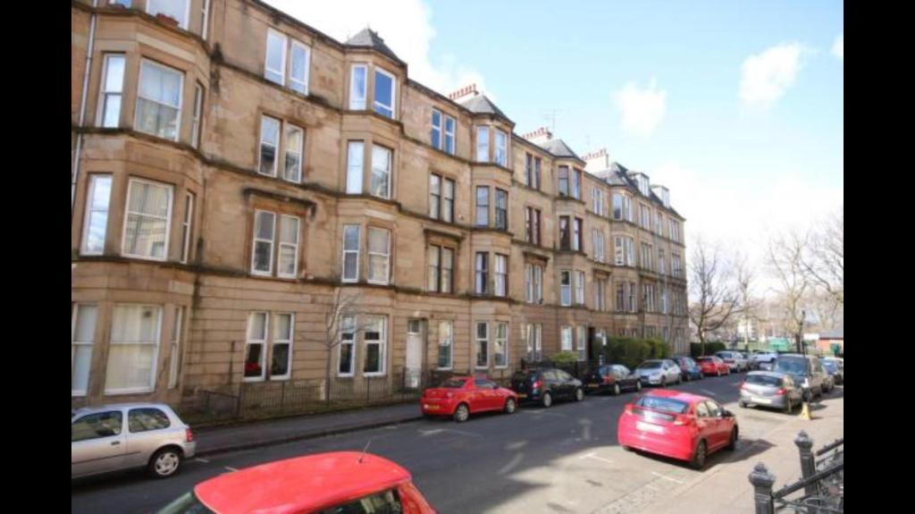 eine Straße mit Autos, die vor einem Gebäude geparkt sind in der Unterkunft Bentinck Street Ground Floor Apartment in Glasgow