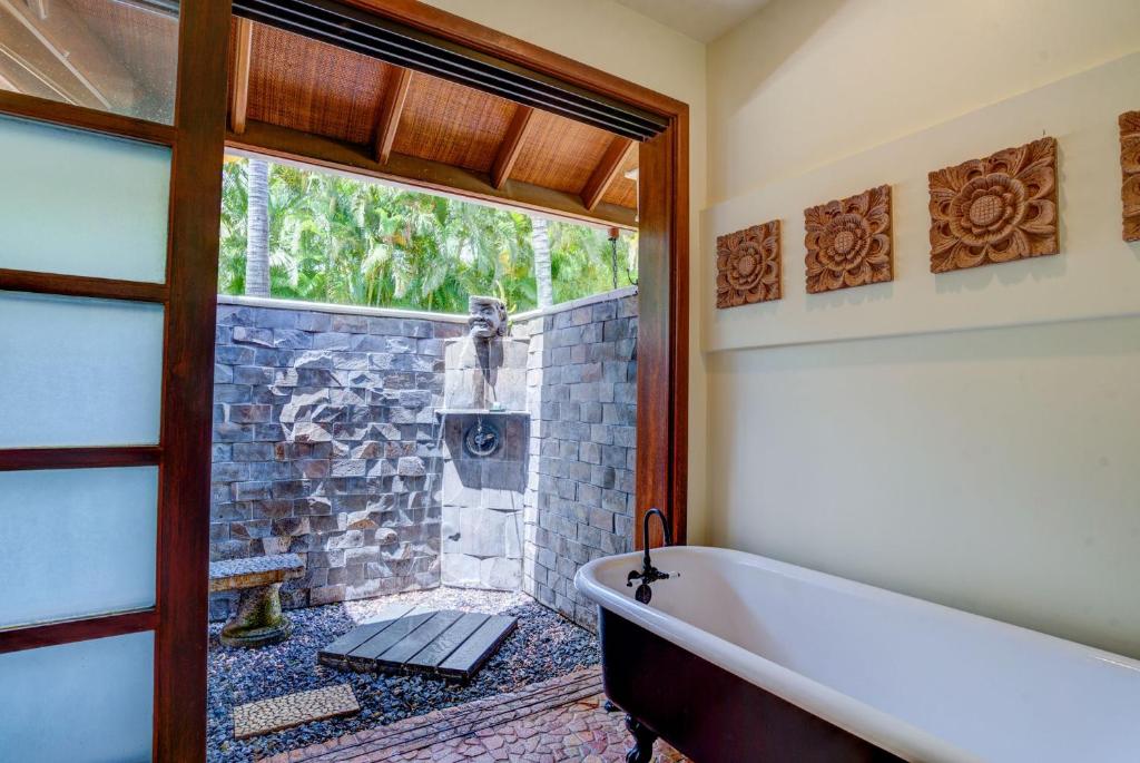 a bathroom with a tub and a stone wall at Ho'oilo House in Lahaina