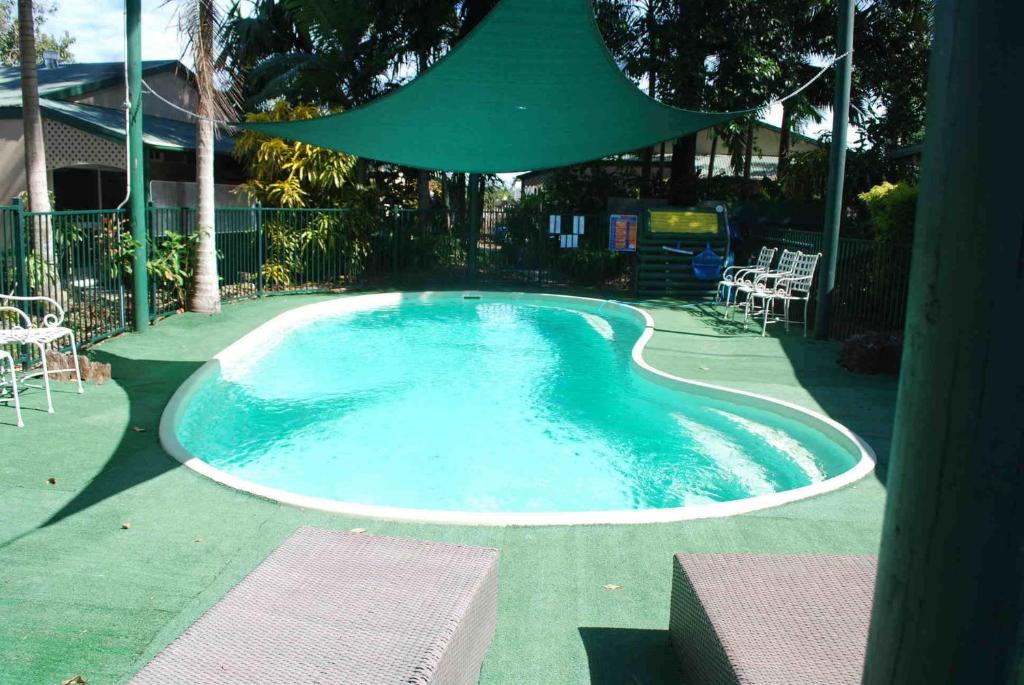 a swimming pool with a green umbrella over it at Rainforest Motel in Mission Beach