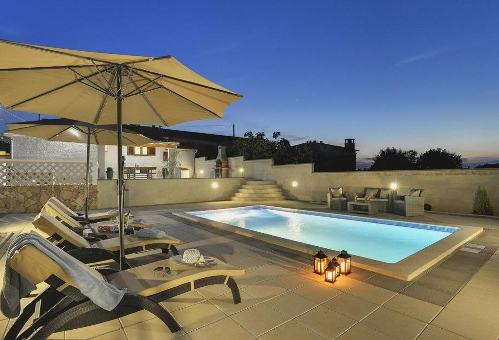 a swimming pool with an umbrella and some chairs and a table at Villa Paola in Vodnjan
