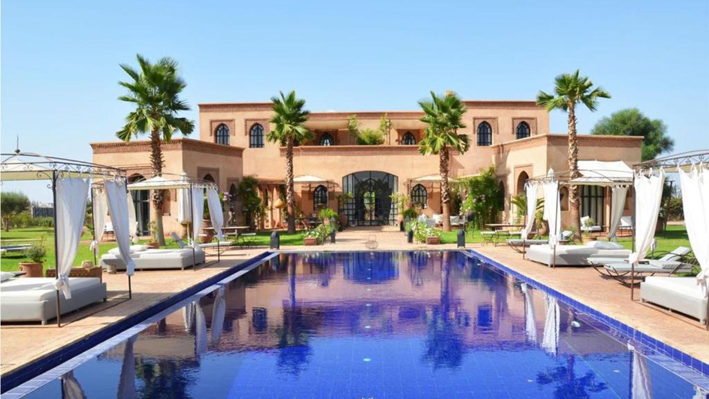 une piscine en face d'un bâtiment avec des palmiers dans l'établissement Palais Lona, à Marrakech