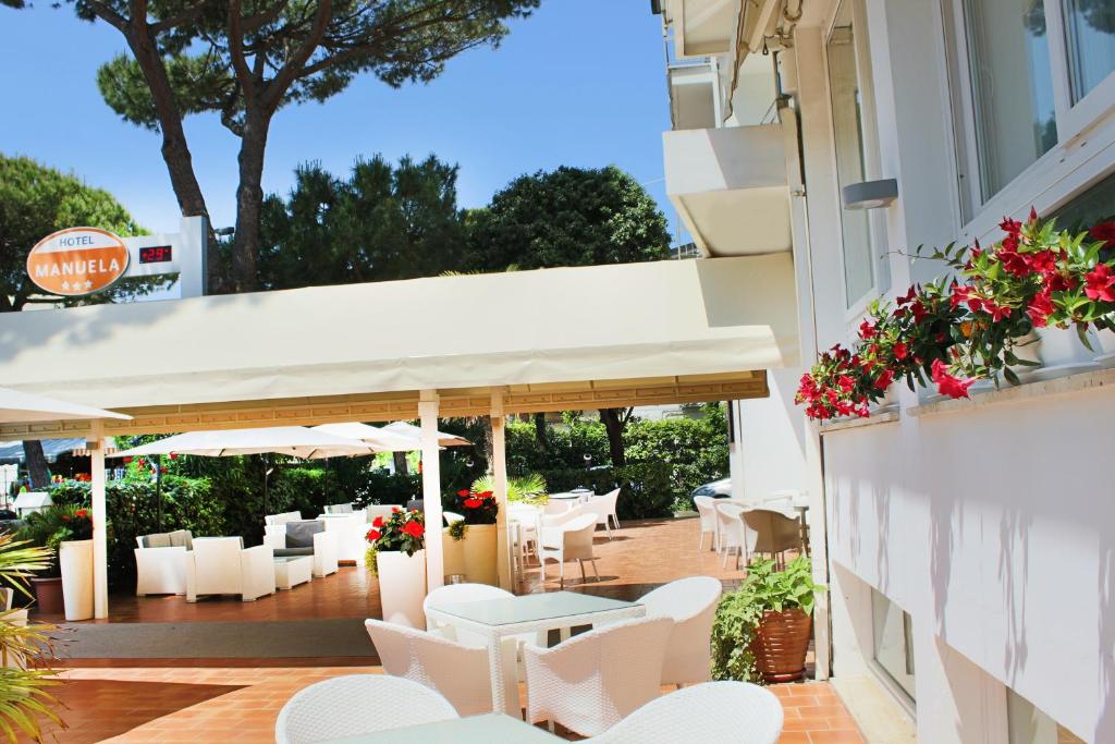 a patio with white chairs and tables and flowers at Hotel Manuela in Cervia