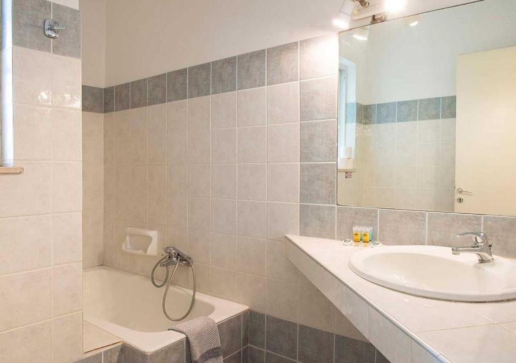 a bathroom with a sink and a tub and a mirror at Stefanakis Hotel & Apartments in Varkiza
