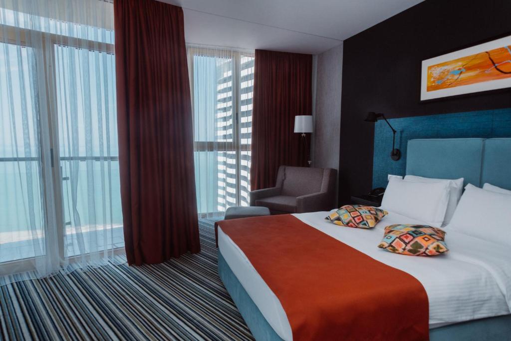 a hotel room with a bed and a chair and windows at Aparthotel Tangerine in Batumi