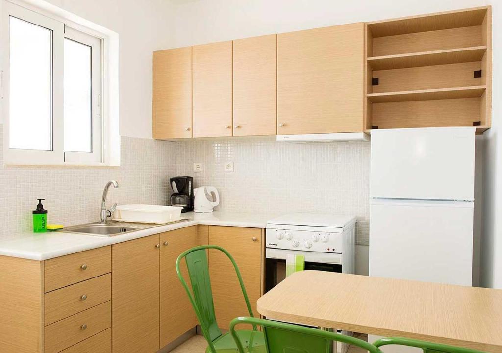 a kitchen with wooden cabinets and a table with green chairs at Stefanakis Hotel & Apartments in Varkiza