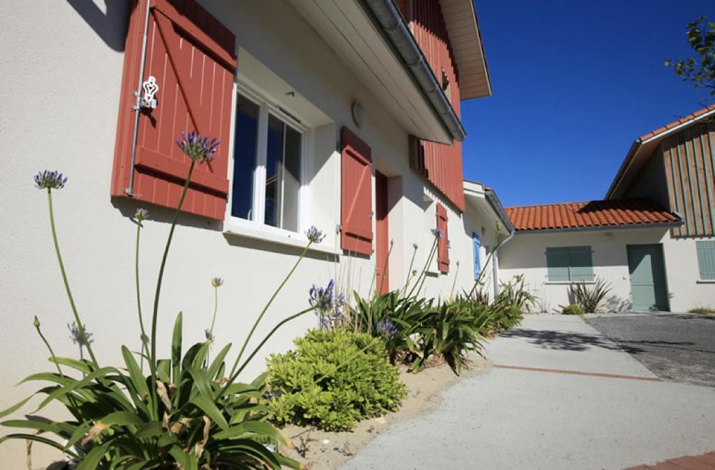 a building with red shutters and plants in a courtyard at Residence Plage Oceane in Biscarrosse-Plage
