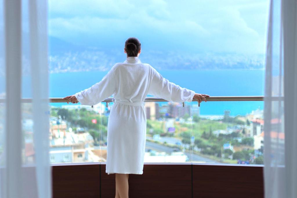 Una mujer con un vestido blanco mirando por la ventana en BURJ ON BAY Hotel, en Jounieh