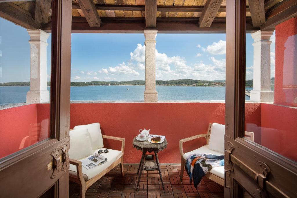 een veranda met een tafel en stoelen en uitzicht op het water bij Hotel Angelo d'Oro in Rovinj