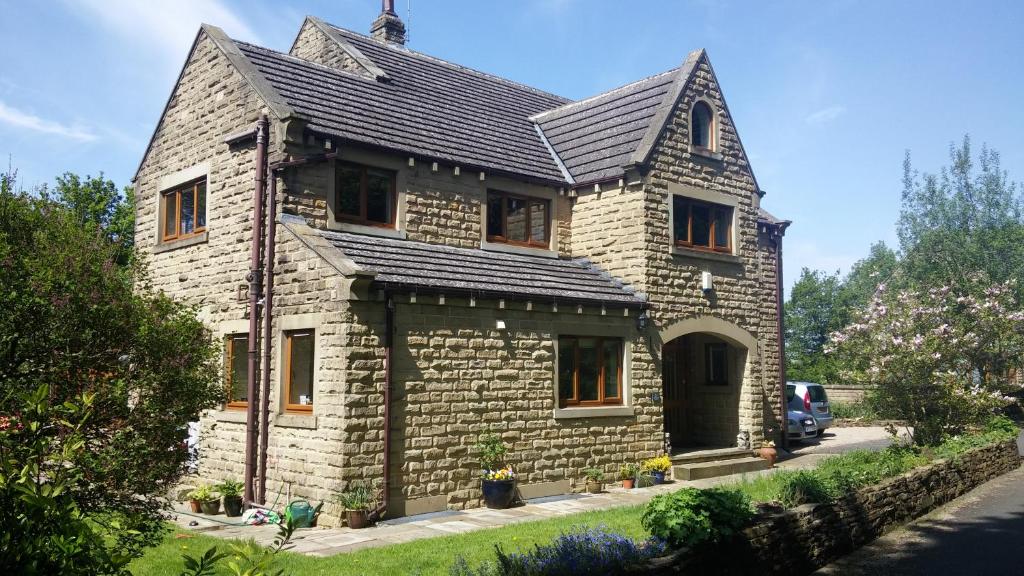 una pequeña casa de piedra con techo negro en Wood Bank Studio Apartment en Holmfirth