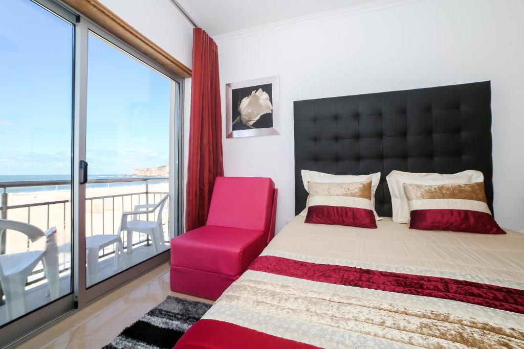 a bedroom with a large bed and a red chair at apartamentos Quebra-Mar in Nazaré